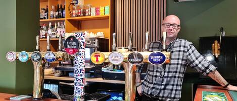 A bar area with multiple beer taps, a counter with a coaster, and shelves stocked with bottles in the background.