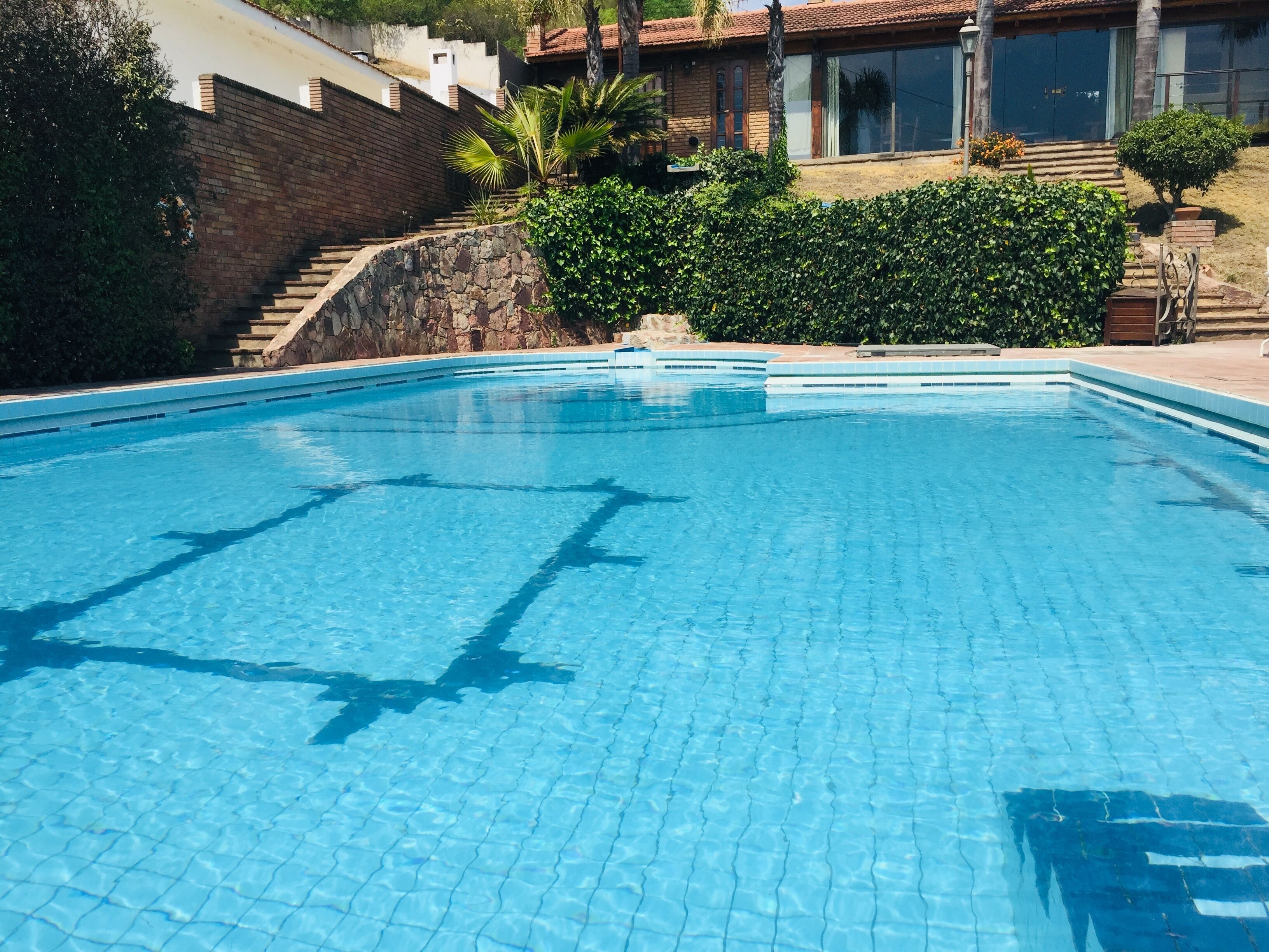 Una piscina cristalina con un muro de piedra y escalones que conducen a un edificio con amplios ventanales.
