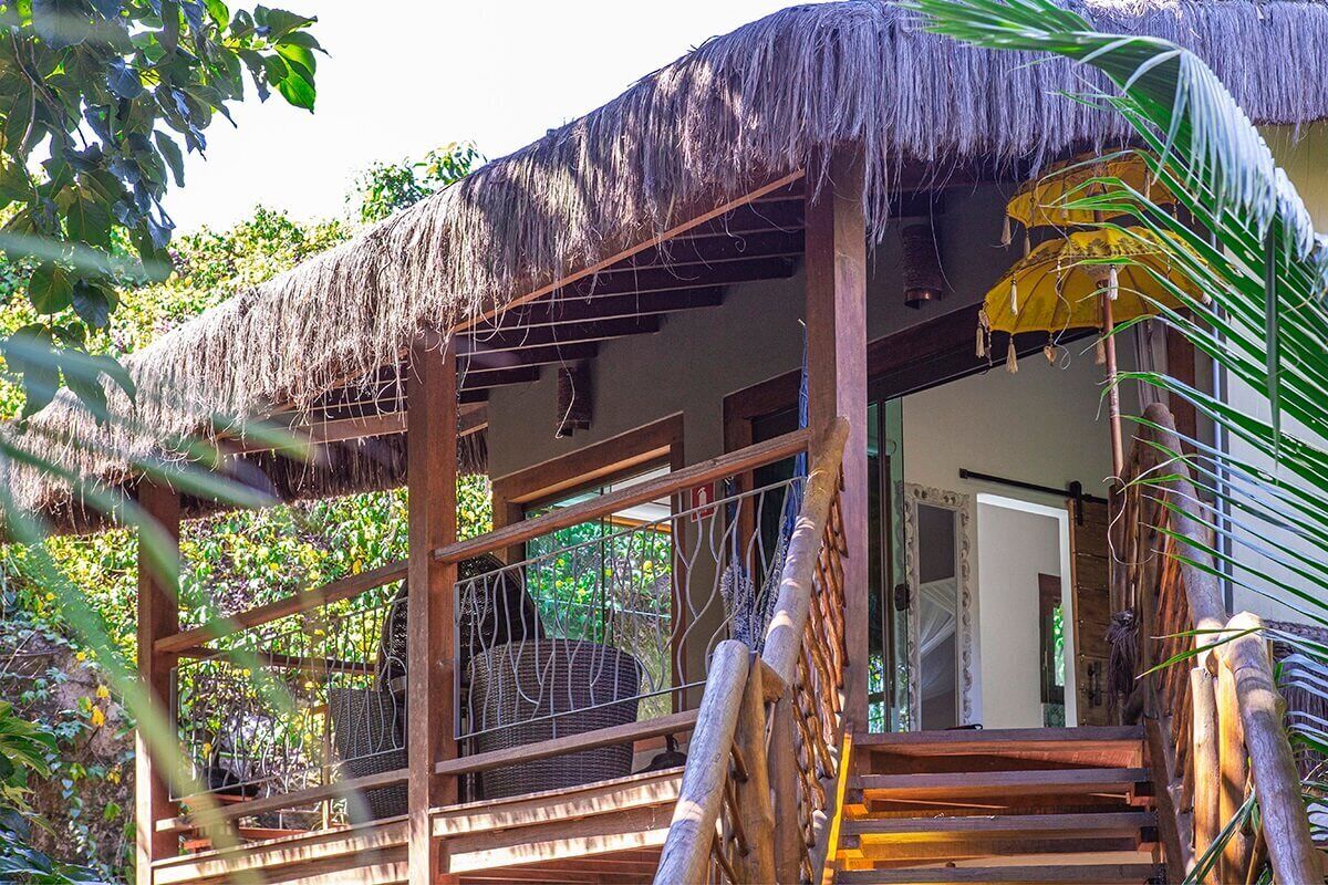 A thatched-roof structure with a wooden balcony, surrounded by lush greenery.