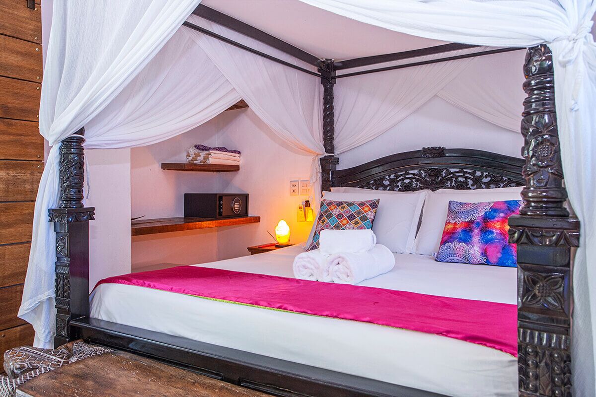 Una cama con dosel, una mesita de noche, una mesilla auxiliar y un estante con objetos decorativos.