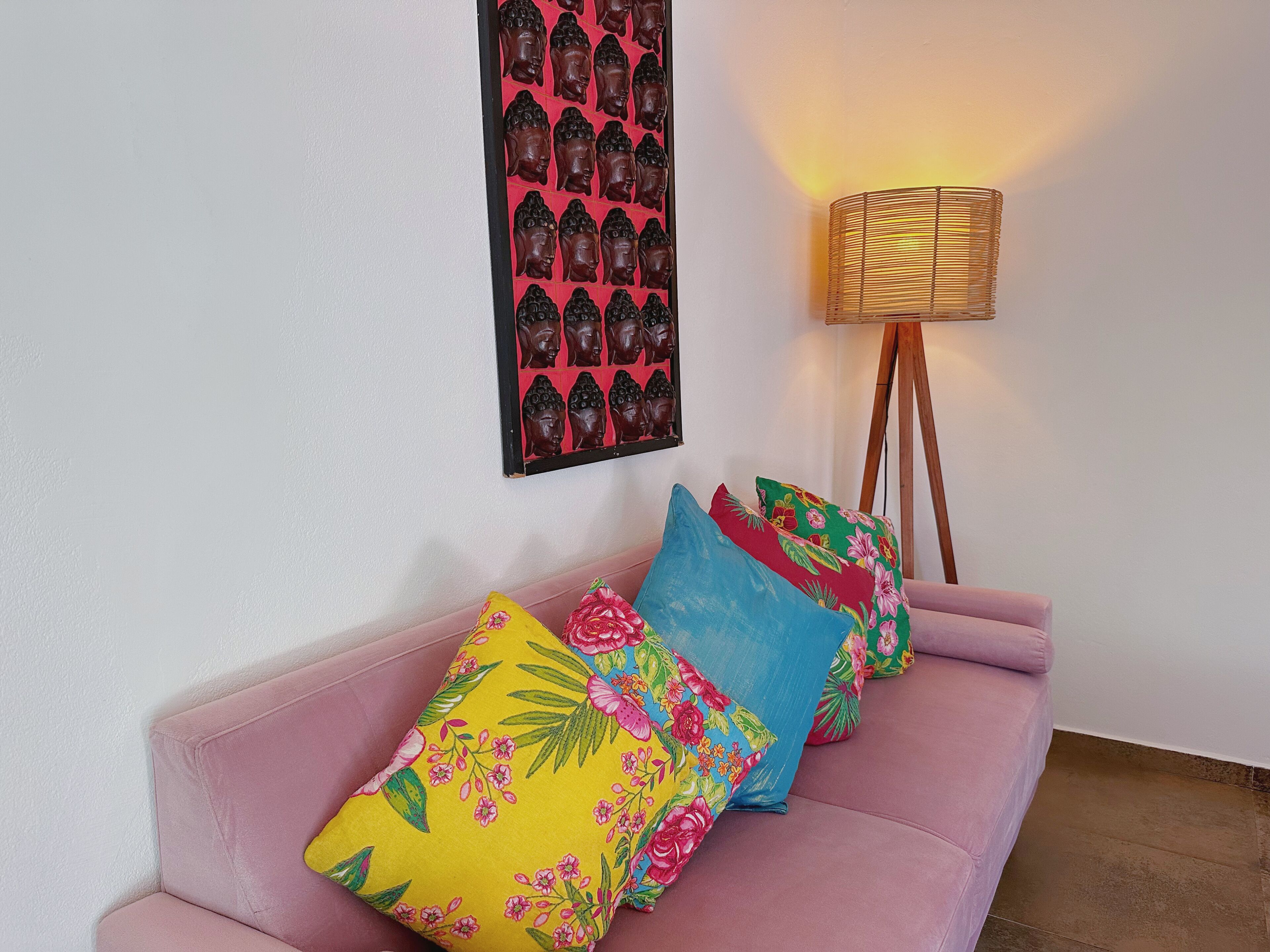 A pink sofa with floral cushions, a wall-mounted Buddha statue, and a floor lamp.