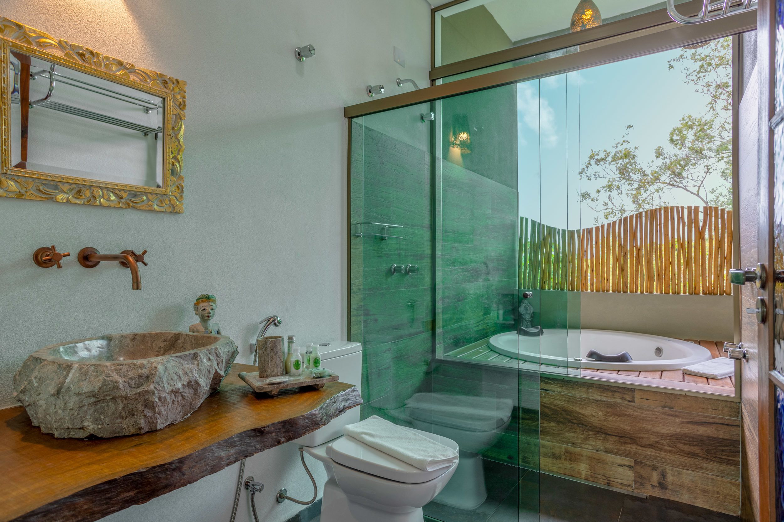 Een badkamer met een stenen wasbak, een houten aanrechtblad, een glazen douchecabine en een wit toilet.