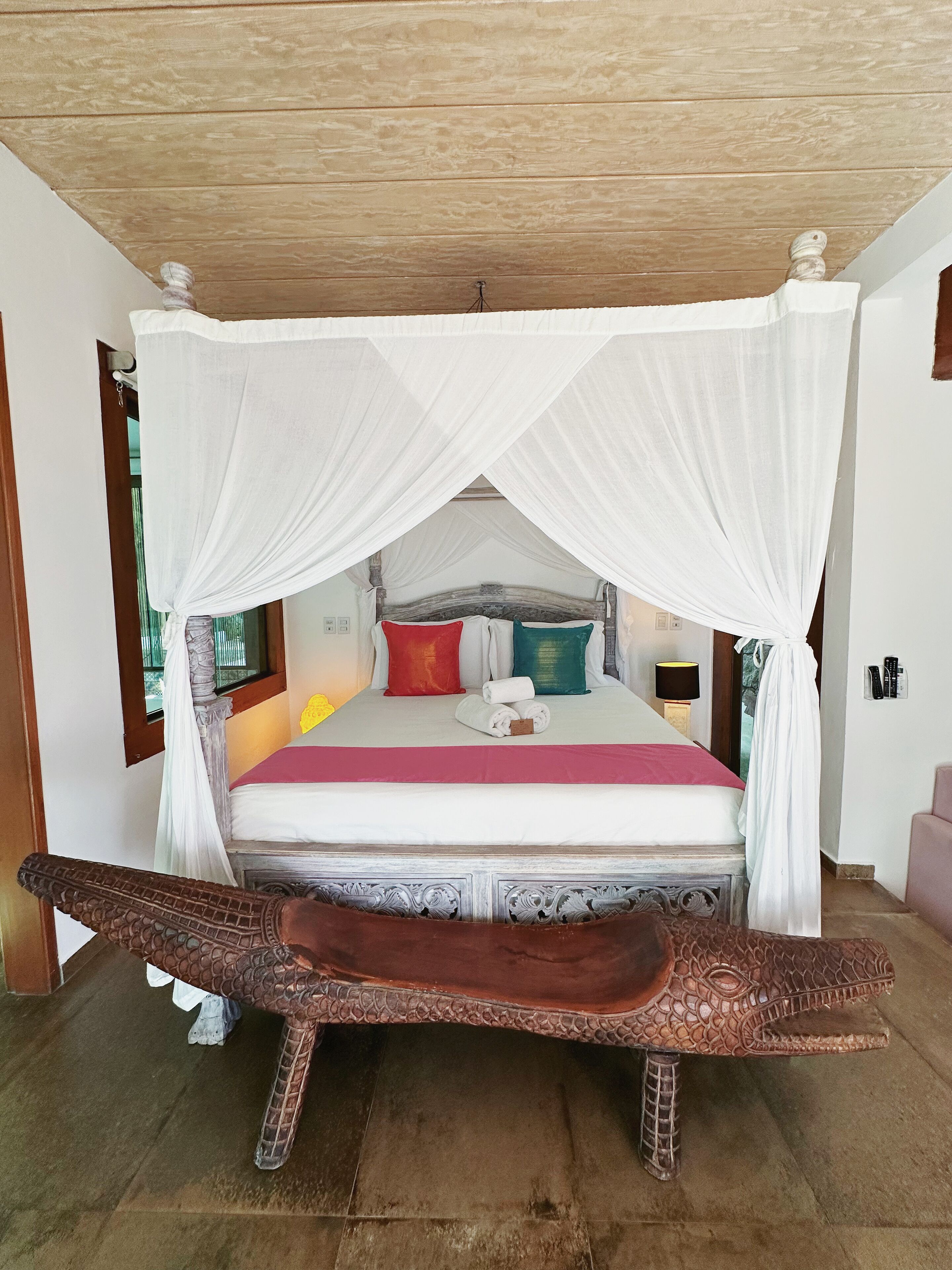 A bed with a canopy, a wooden headboard, and a decorative bench in front.