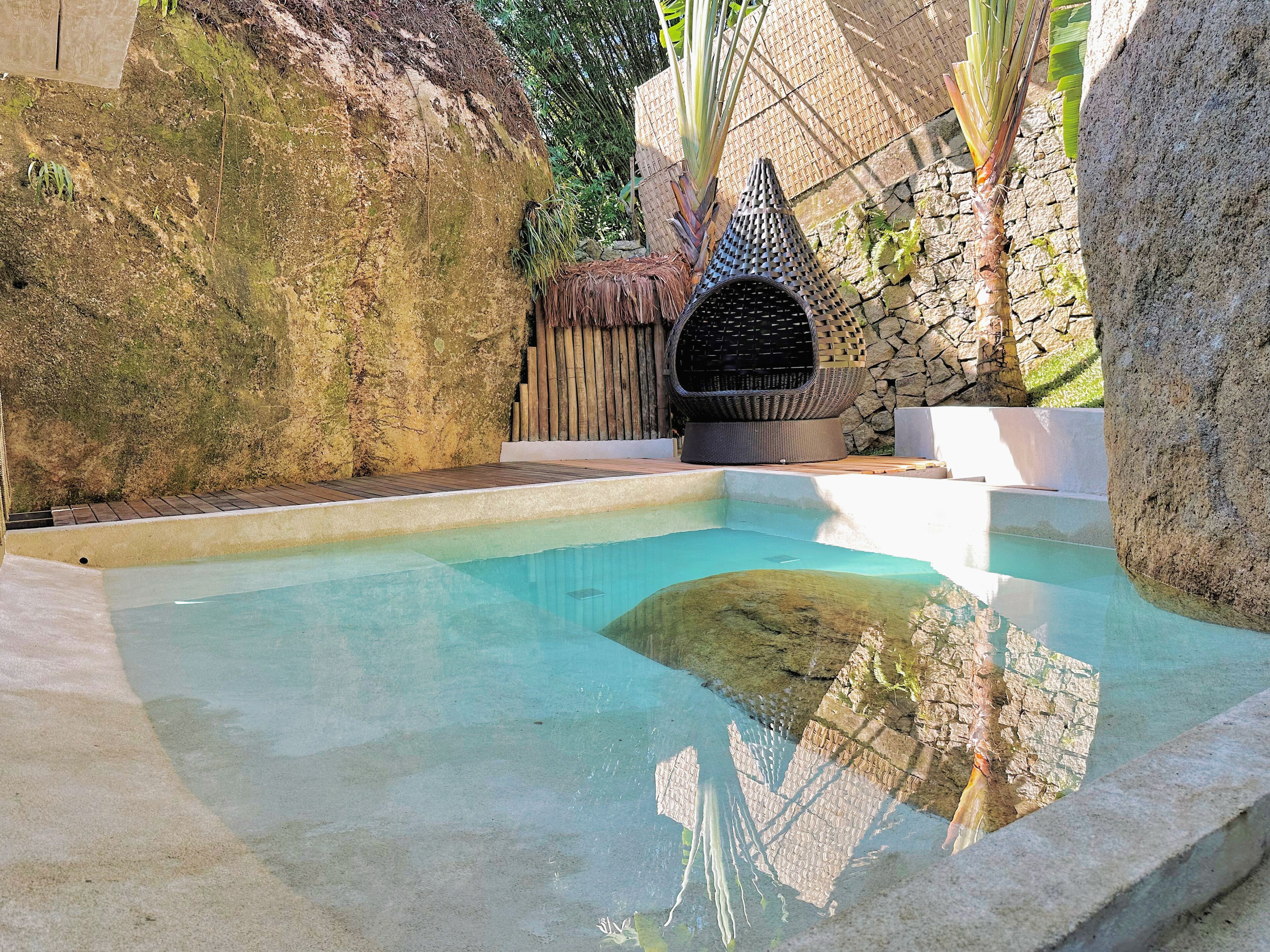 A swimming pool with a stone wall and a thatched-roof structure.