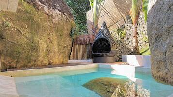 A swimming pool with a stone wall and a thatched-roof structure.