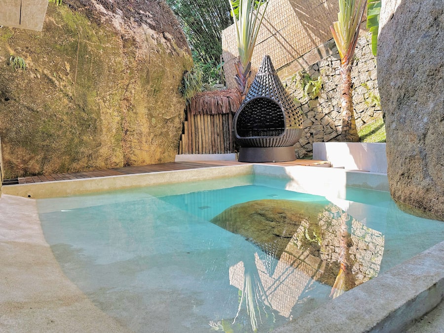 A swimming pool with a stone wall and a thatched-roof structure.