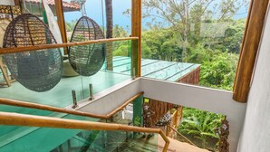 A modern interior with a glass staircase, hanging chairs, and a view of lush greenery. - Hotel Vila Kebaya (Ilhabela)