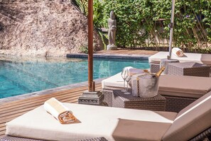 Zona junto a la piscina con sillones de descanso, una estatua y una botella de champán.
