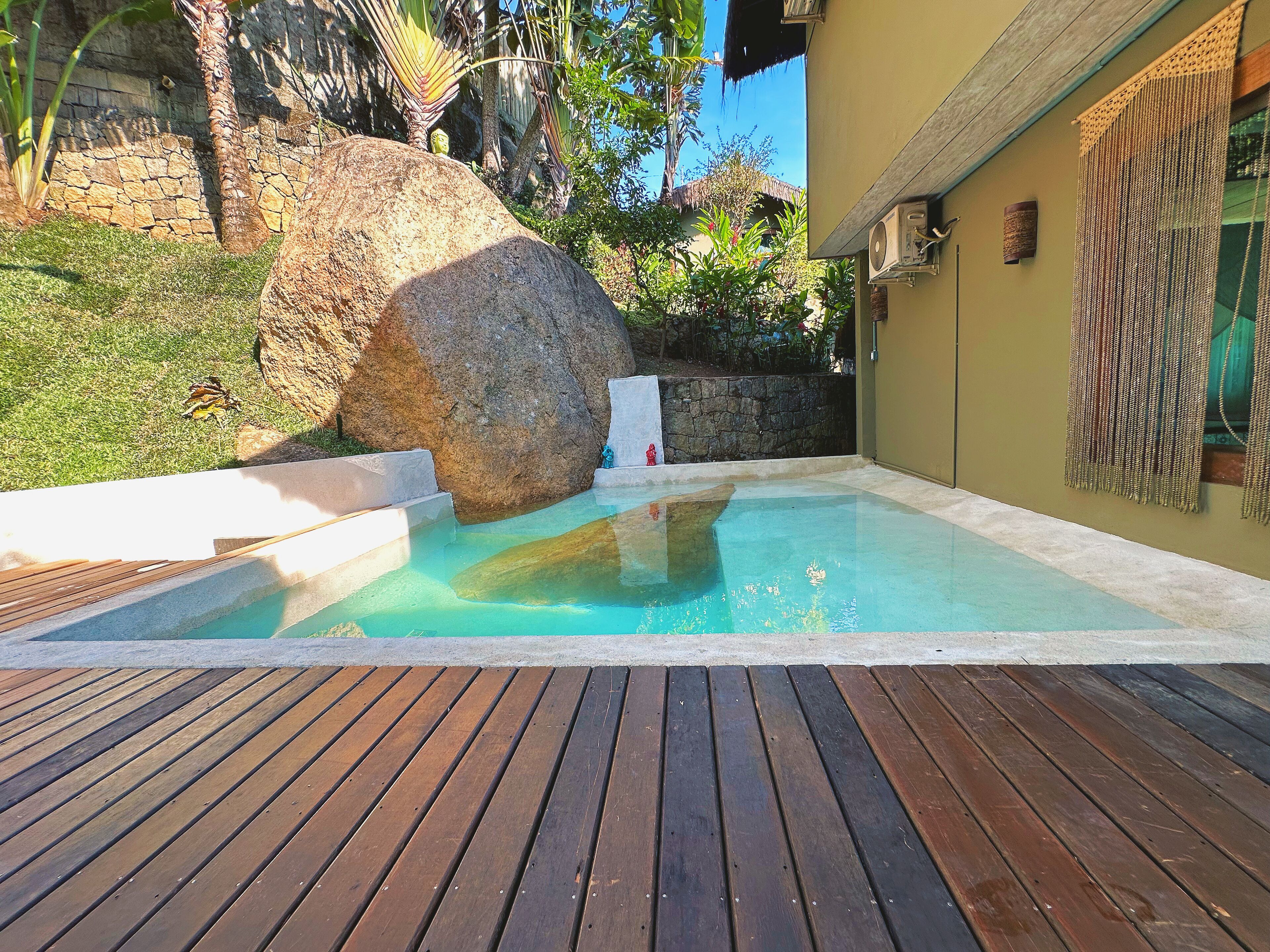 A swimming pool with a wooden deck, a large rock, and a stone wall.