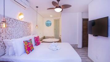 A hotel room with a bed, a ceiling fan, a TV, and a bathroom with a round mirror.