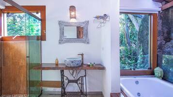 A bathroom with a large bathtub, a sink with a decorative bowl, a mirror, and a shower area.