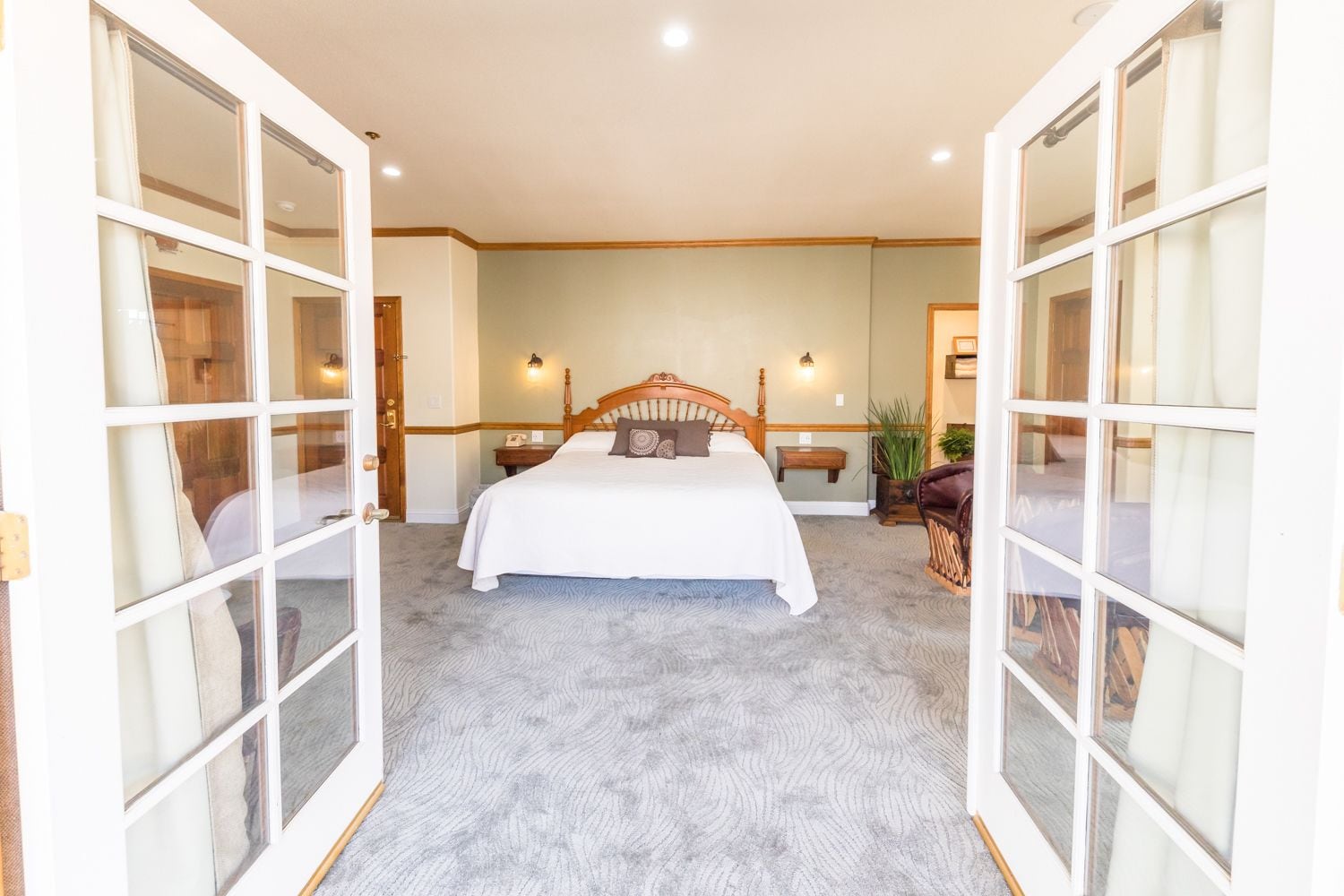 A bedroom with a large bed, two bedside tables, a nightstand, a chair, and a potted plant.