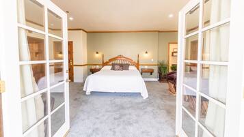 A bedroom with a large bed, two bedside tables, a nightstand, a chair, and a potted plant.