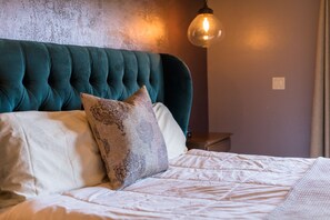 A neatly made bed with a tufted headboard, a patterned pillow, and a bedside lamp. - Posada De San Juan (San Juan Bautista)