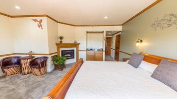 A bedroom with a bed, a desk with chairs, a fireplace, a bathroom, and a hallway.