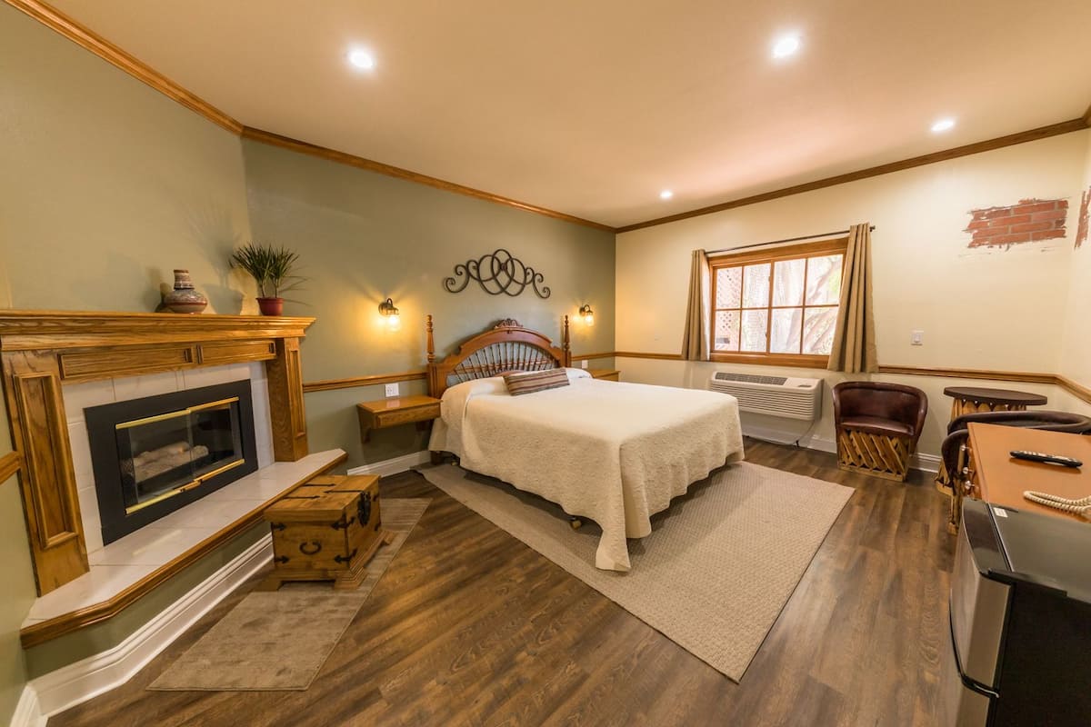 A bedroom with a fireplace, a bed, a nightstand, a chair, a table, and a window.