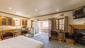 A hotel room with a bed, a TV, a fireplace, and a balcony with chairs.