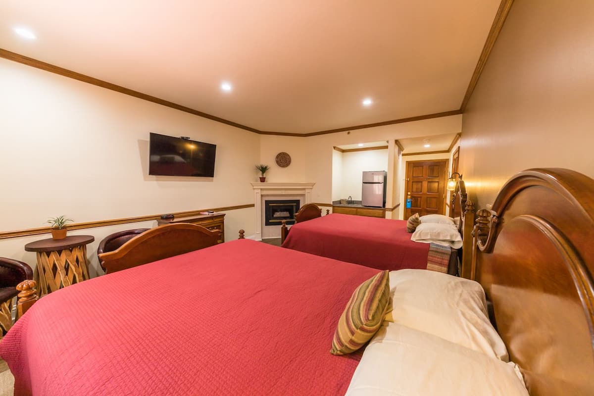 A hotel room with two beds, a fireplace, a TV, and a small kitchen area.