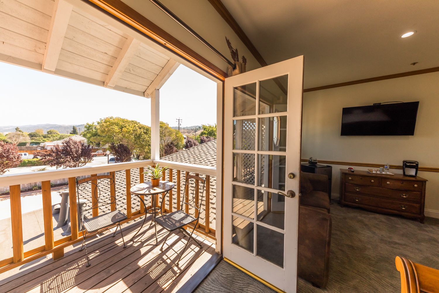 Un balcon avec une balustrade en bois, une petite table avec une plante et une vue sur l’extérieur.