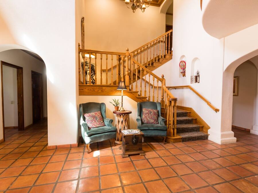 Uma sala de estar ampla com escada de madeira, dois poltronas com almofadas florais e uma pequena mesa com abajur.