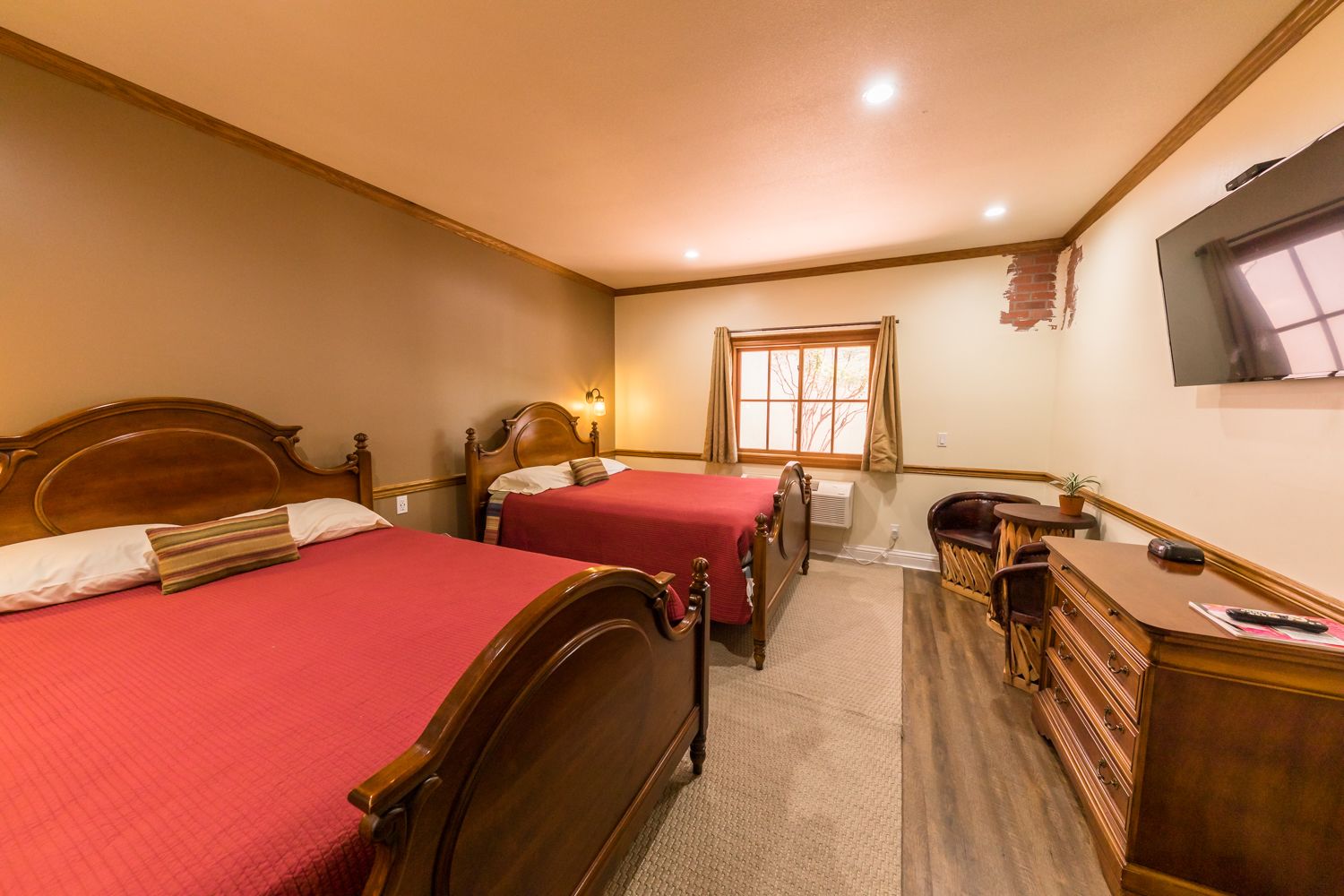 Una habitación de hotel con dos camas de madera, un escritorio, una silla, un televisor y una ventana con cortinas.