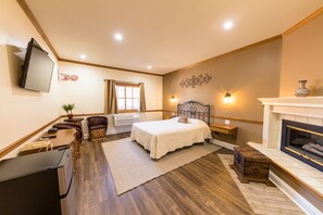 A hotel room with a bed, a desk, a chair, a TV, a fireplace, and a window.