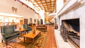 A spacious lobby with a fireplace, wooden furniture, and a high ceiling with exposed beams.
