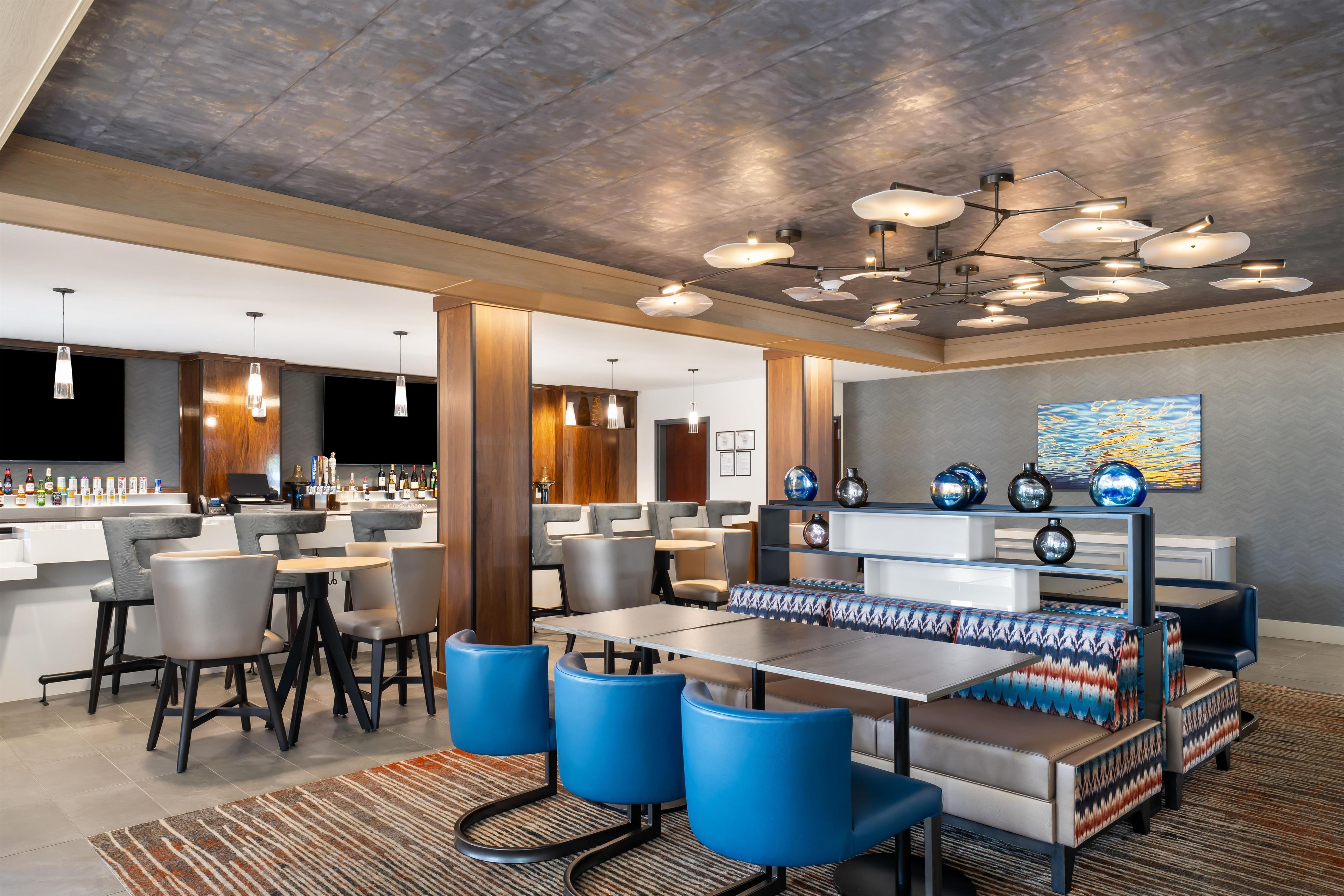 A modern hotel lobby with a bar area, seating arrangements, and a unique ceiling design.
