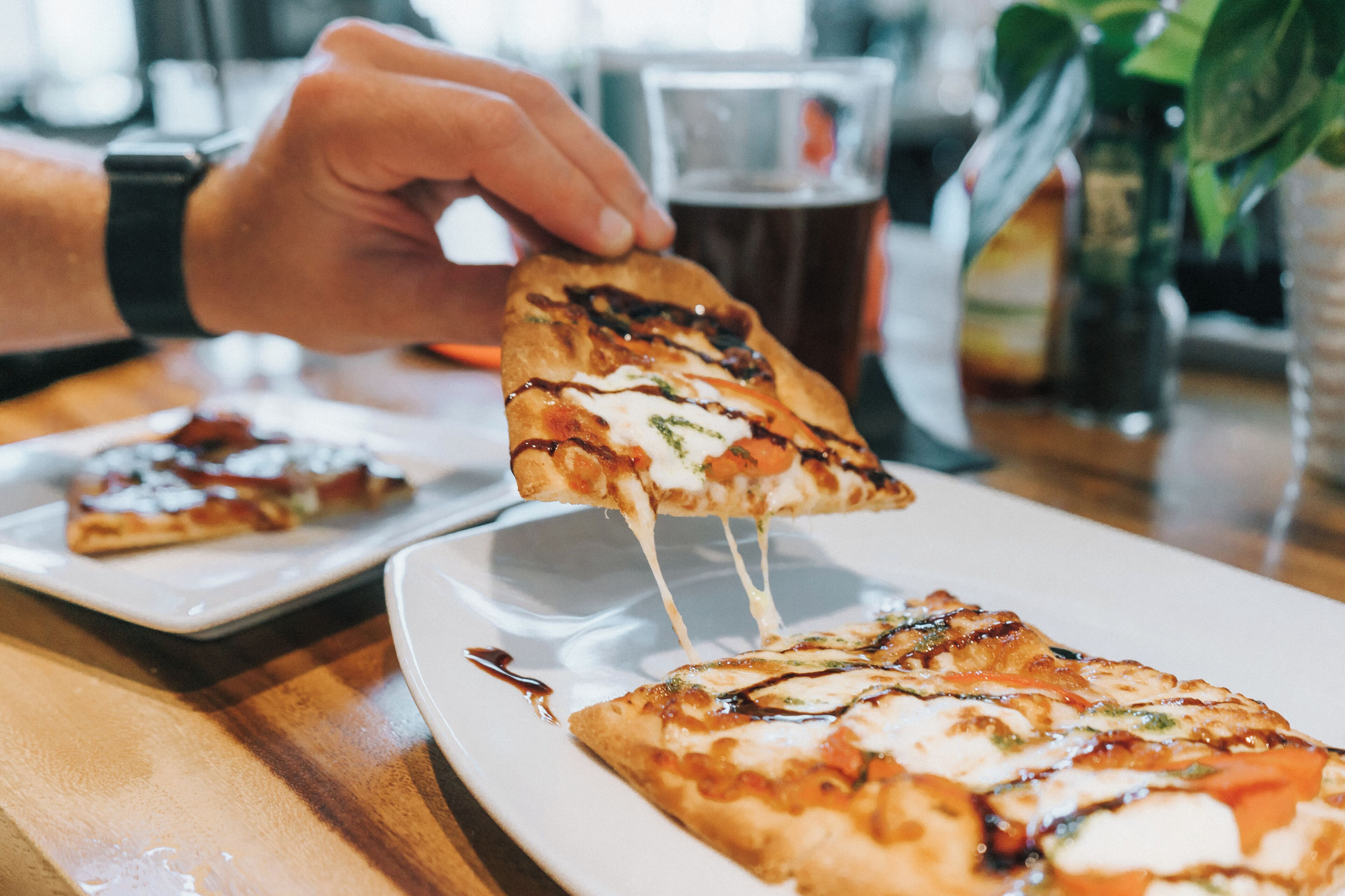 A hand holding a slice of pizza with melted cheese, on a white plate.