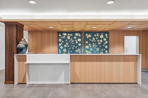 A reception desk with a wooden finish, a blue wall with a leaf pattern, and a white door. - Hyatt House Orlando International Drive (Orlando)