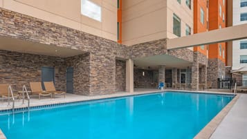 A swimming pool with a stone facade, lounge chairs, and a covered seating area.