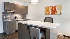 Une cuisine moderne avec des meubles gris, un plan de travail blanc et un îlot central doté d’un tabouret.