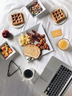 Un assortiment de mets pour le petit-déjeuner est disposé sur une table : des gaufres, des œufs brouillés, du bacon, des toasts et des fruits.