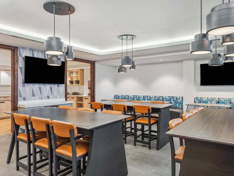Een moderne eetruimte met meerdere tafels en stoelen, verlichting aan het plafond en een keuken op de achtergrond.