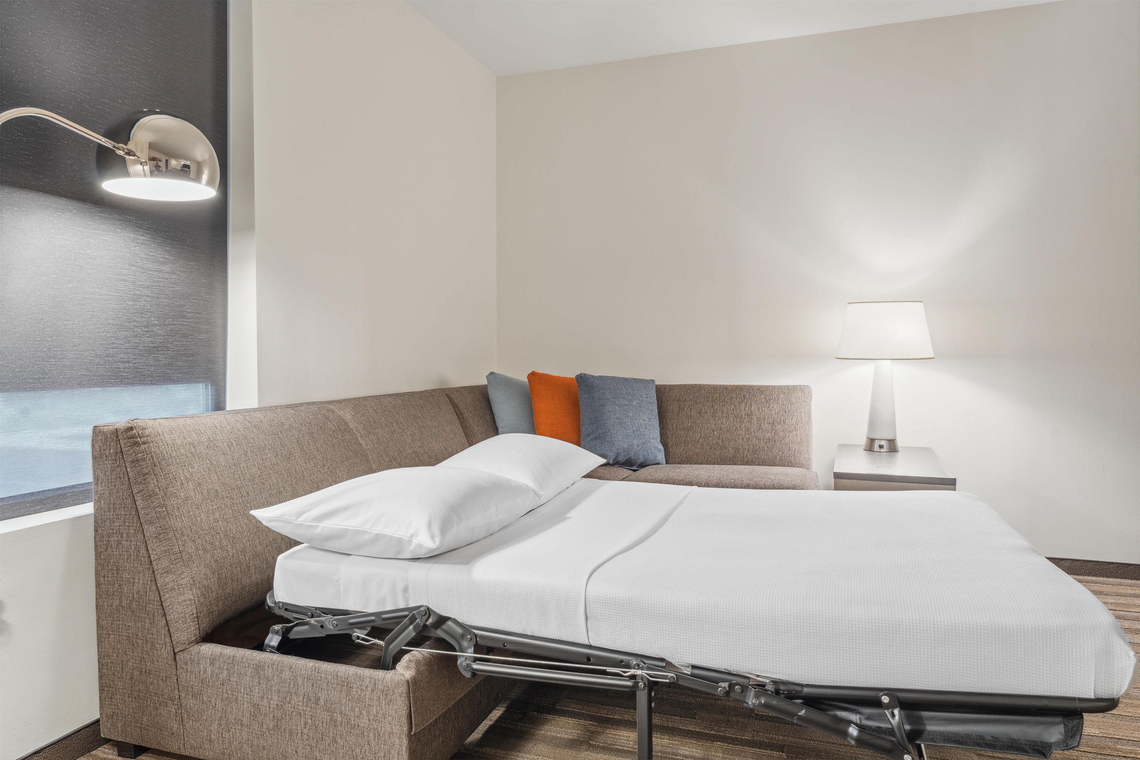 Una habitación de hotel moderna con un sofá cama plegable, una lámpara de noche y vistas al exterior.