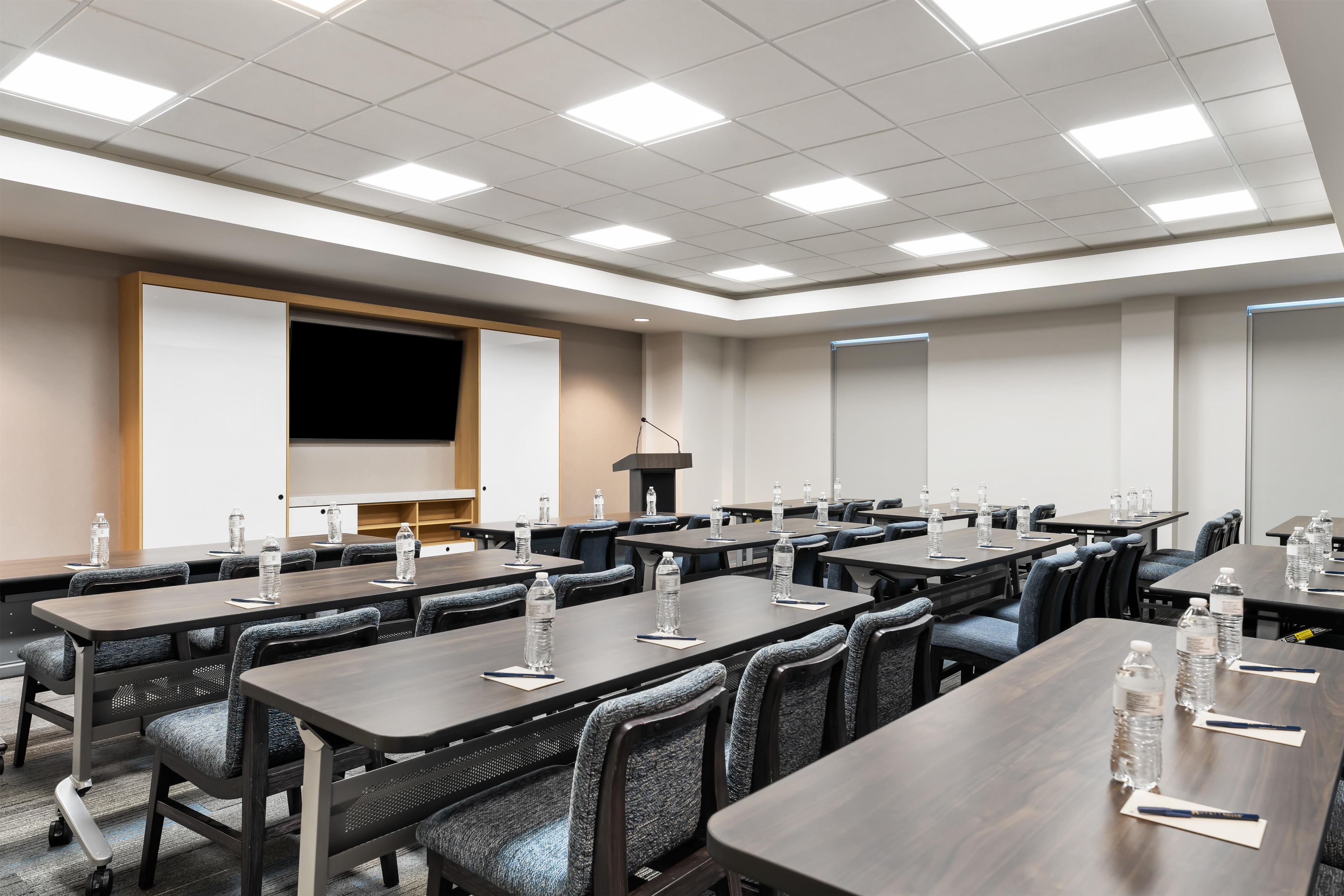 A conference room with multiple tables, chairs, and a large screen.
