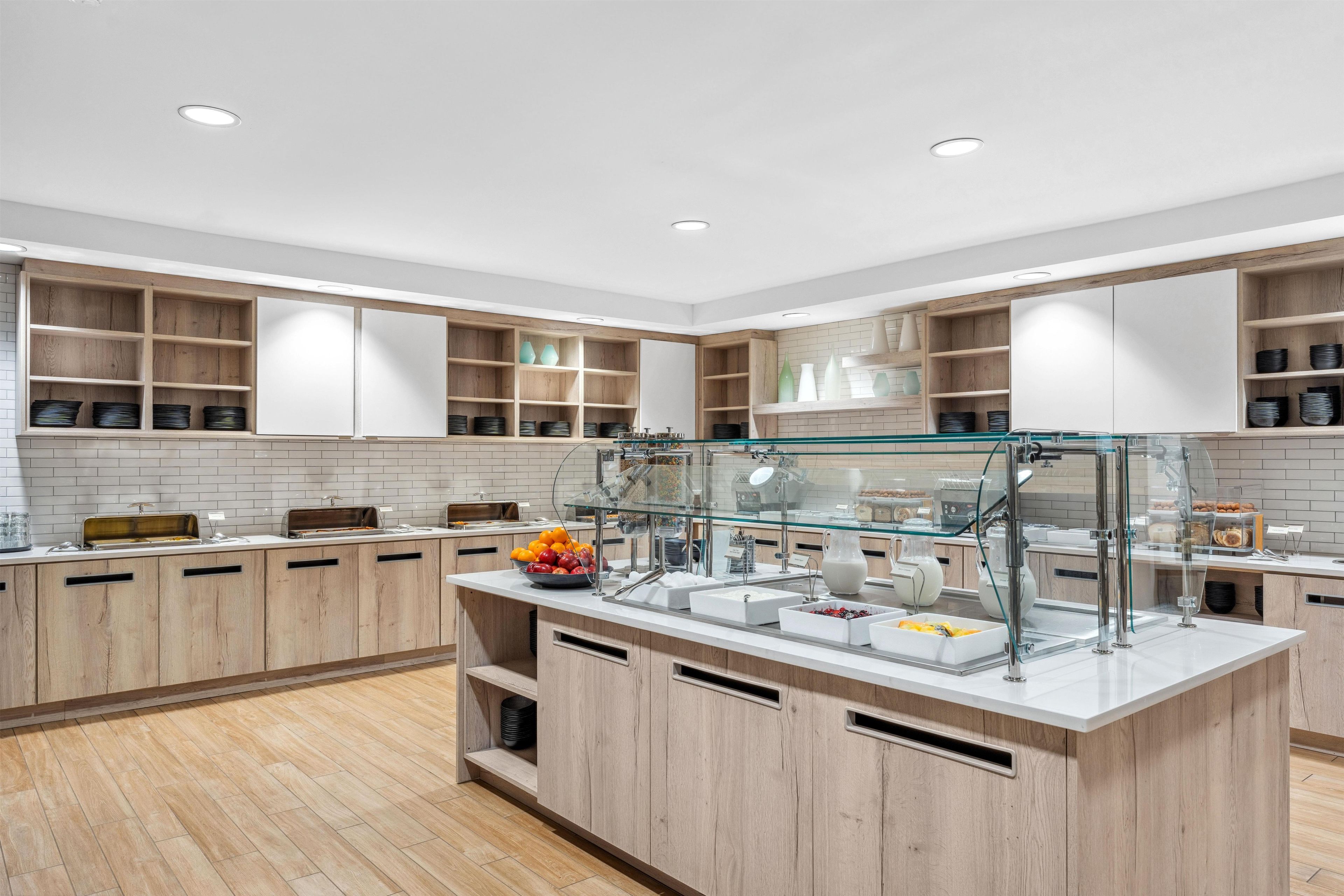 Una cocina moderna con gabinetes de madera, una vitrina de vidrio y un salpicadero blanco de azulejos.