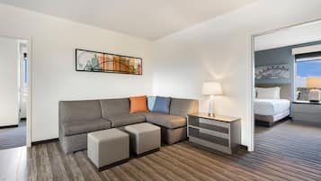 A hotel room with a sectional sofa, a bedside table with a lamp, and a bed with a headboard.