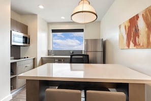 Una cocina moderna con una isla grande, electrodomésticos de acero inoxidable y vistas al cielo a través de una ventana.