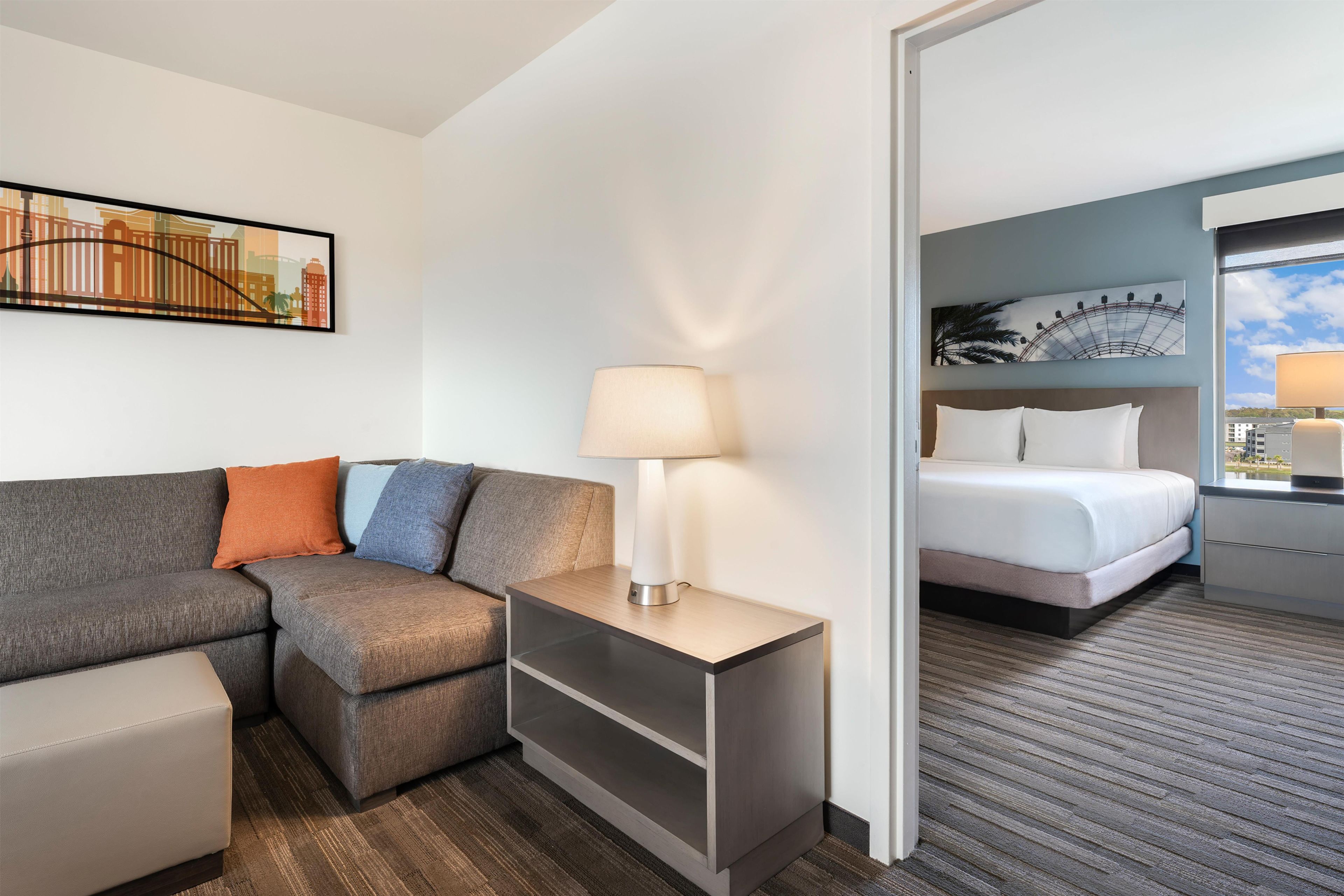 Ein Hotelzimmer mit Sofa, Nachttisch mit Lampe, Bett und einem Bild an der Wand.