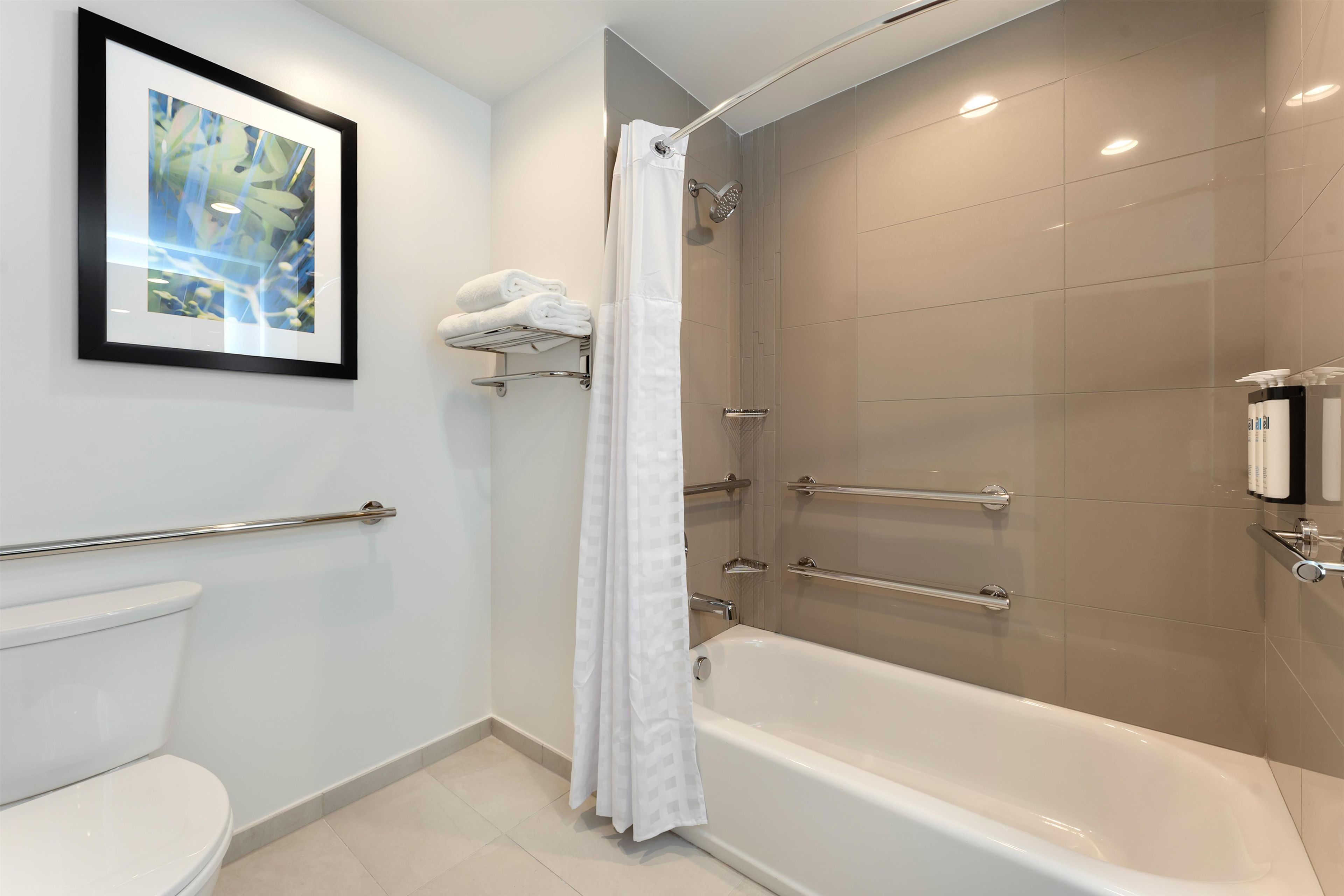 A modern bathroom with a toilet, a framed picture on the wall, a shower with a glass door, and a bathtub.