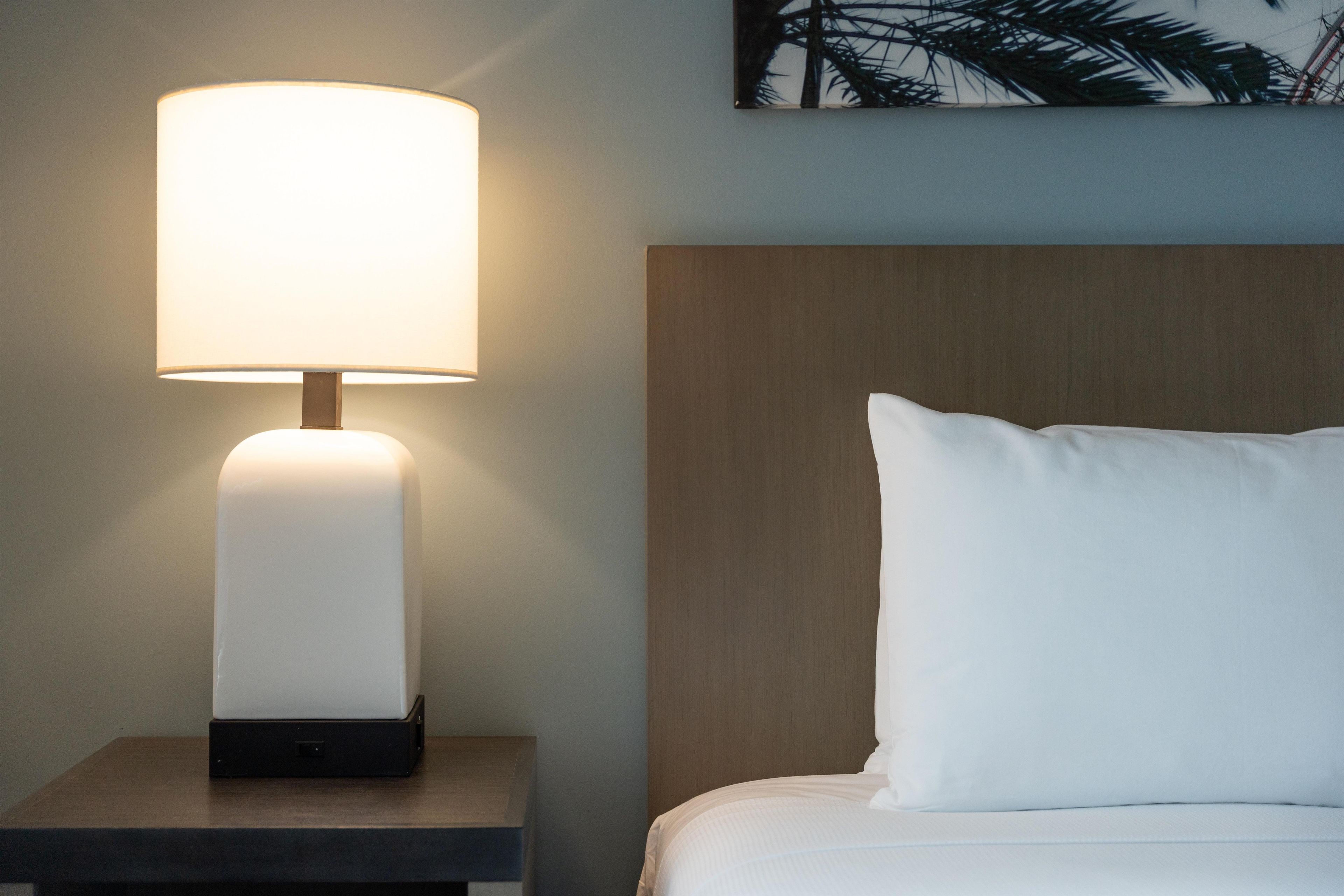 Ein ordentlich bezogenes Bett mit einem weißen Kopfkissen und einem Nachttisch mit einer Lampe.