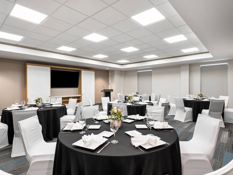 Un salón de conferencias con mesas redondas, sillas blancas y una pantalla de presentación.