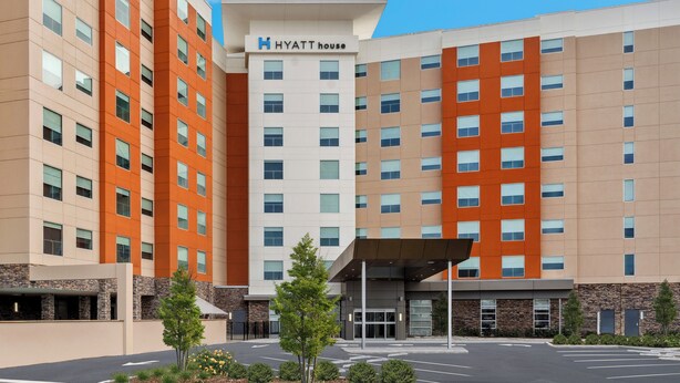 Un hôtel à plusieurs étages, reconnaissable à son grand panneau « Hyatt House », doté d’une entrée couverte et d’un parking aménagé avec des espaces verts.