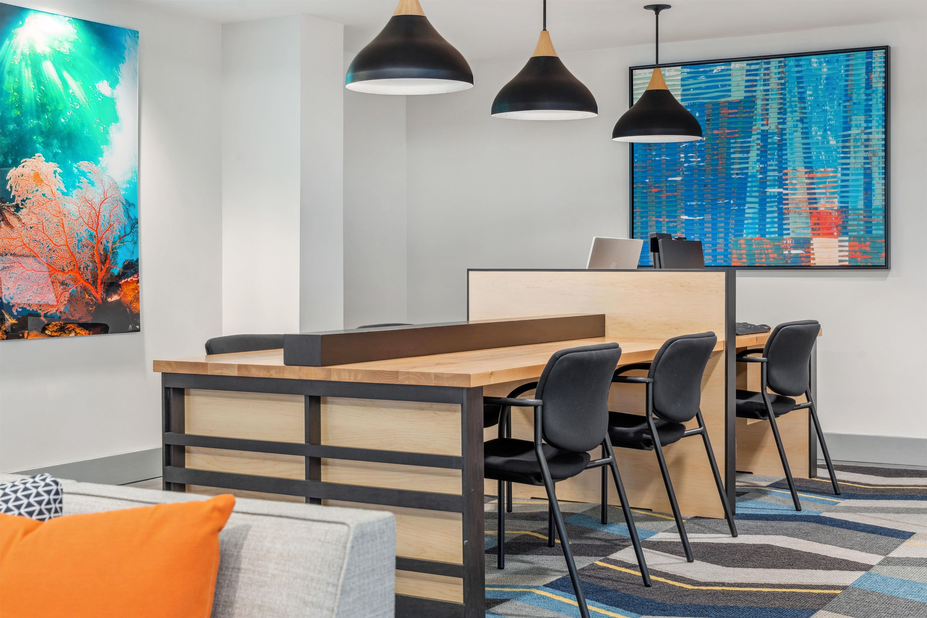 A modern office space with a wooden desk, black chairs, and pendant lighting.
