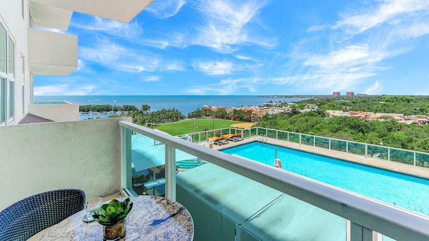 A balcony with a view of a swimming pool, a grassy area, and distant buildings. - iCoconutGrove Vacation Rentals (Miami)