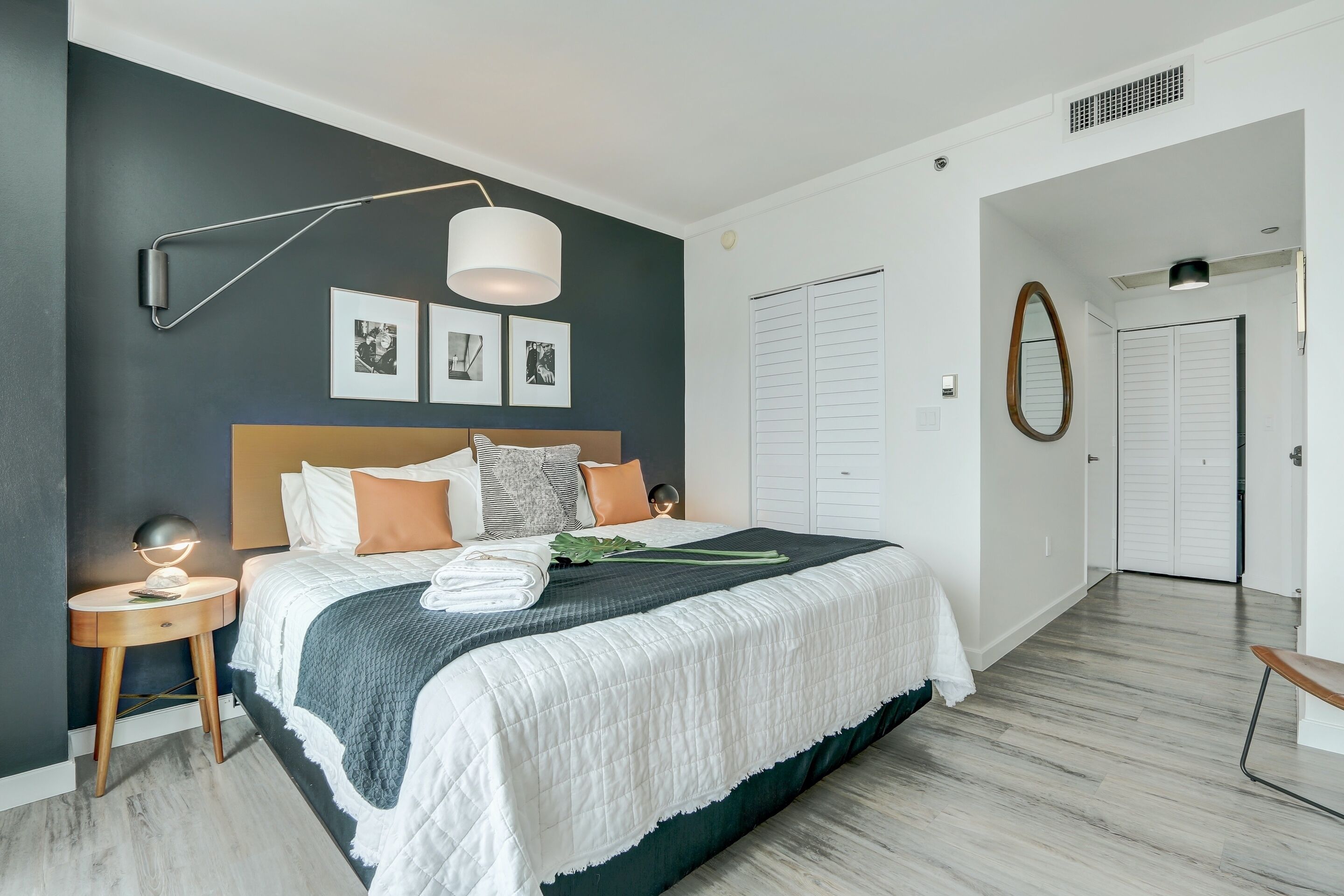 A modern bedroom with a large bed, a bedside table, a lamp, and a wall-mounted picture frame.