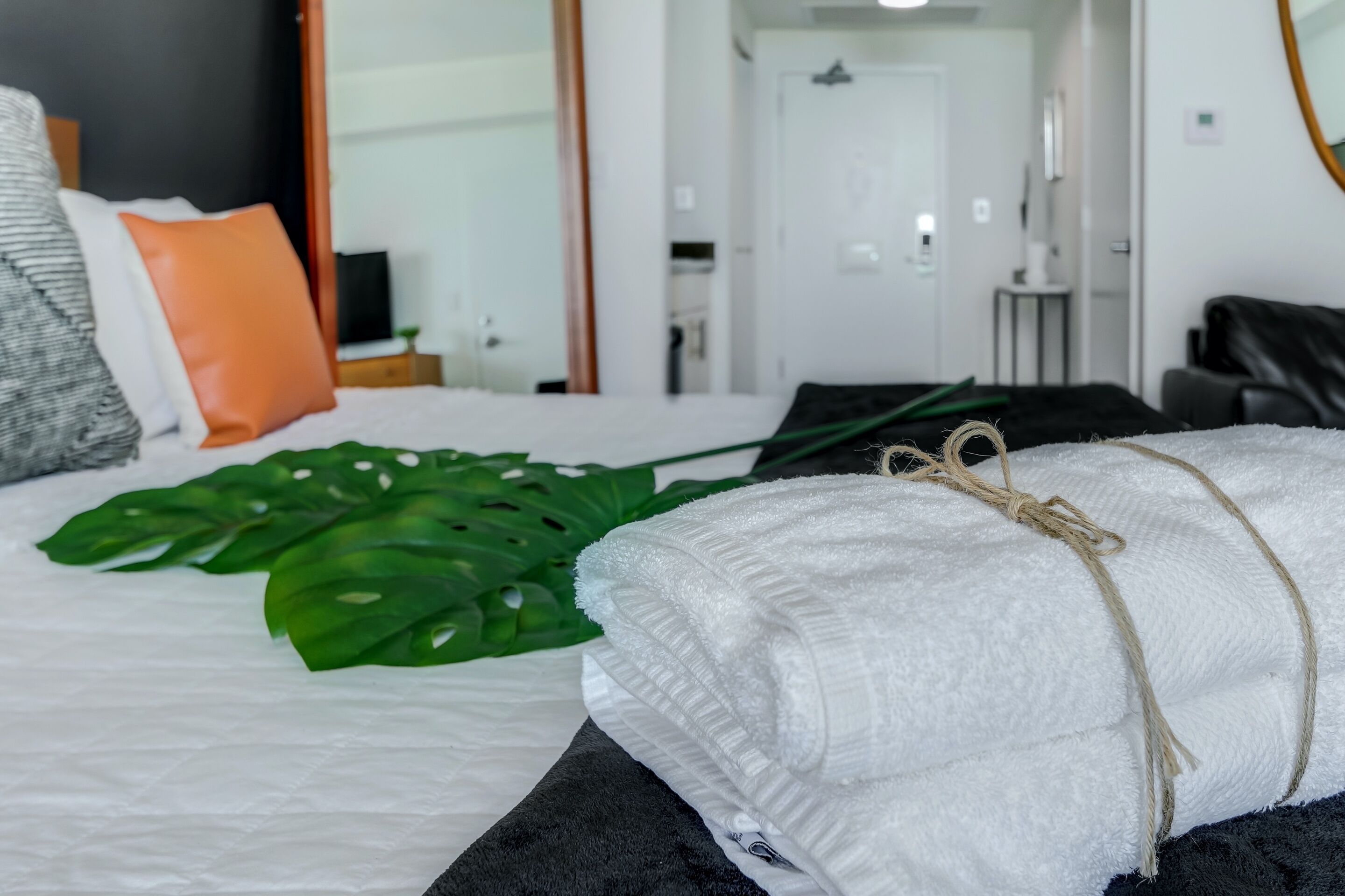 Ein ordentlich bezogenes Bett mit weißem Handtuch, einer großen grünen Pflanze und einem schwarzen Kopfteil.