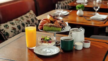 A dining table with a glass of orange juice, a plate with a dessert, a green mug, and small bowls of condiments.