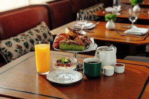 A dining table with a glass of orange juice, a plate with a dessert, a green mug, and small bowls of condiments. - Shinola Hotel (Detroit)